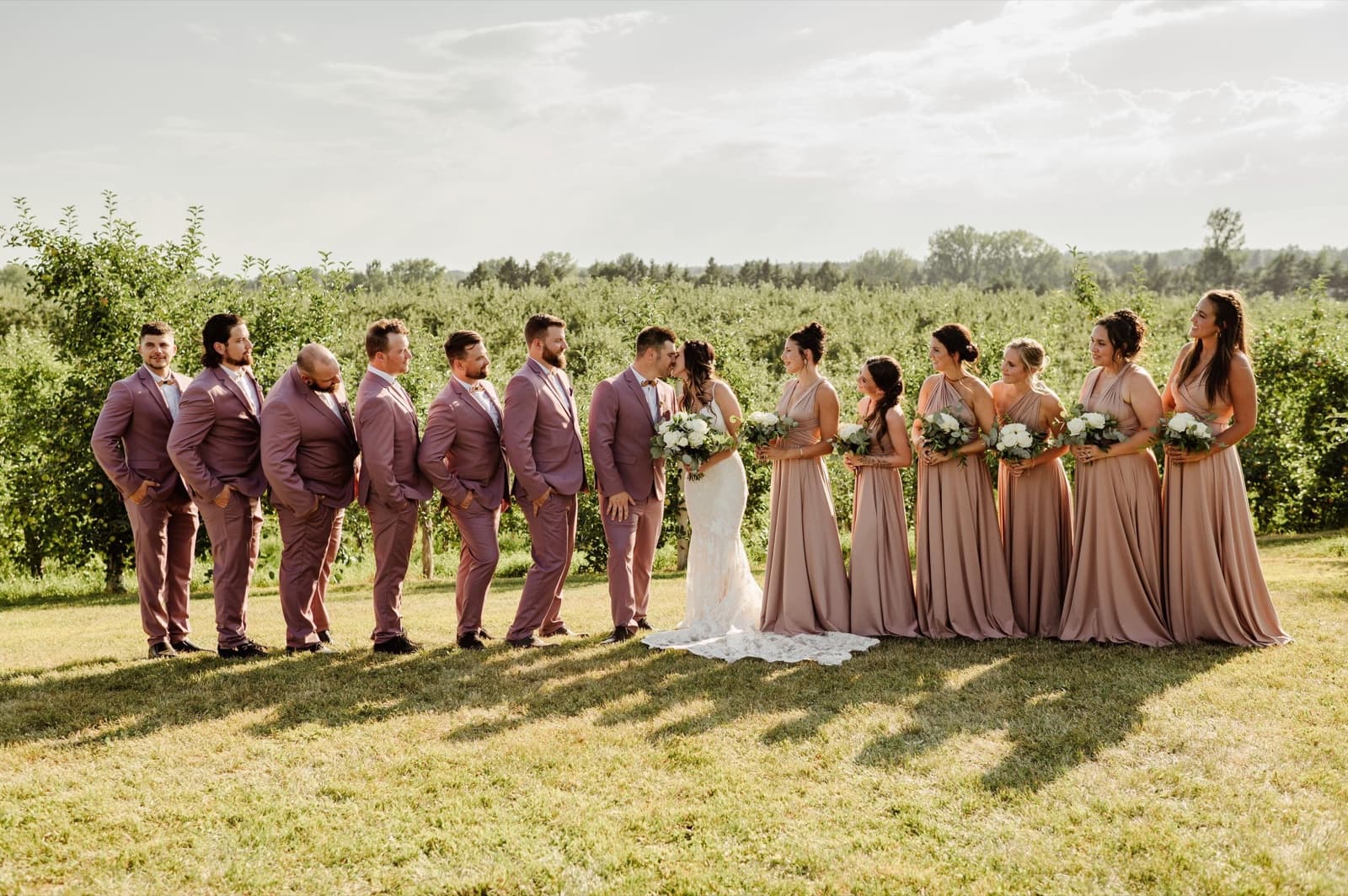 Cortège de mariage au complet dans le verger, robes dusty rose et costumes assortis